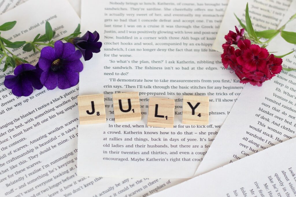 JULY written in letters, with flowers around. Background: book pages.